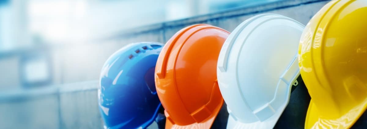 A close-up of four construction safety hard hats lined up together in blue, orange, white, and yellow.