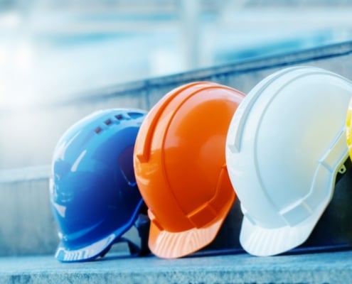 A close-up of four construction safety professional hard hats lined up together in blue, orange, white, and yellow.