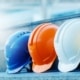 A close-up of four construction safety hard hats lined up together in blue, orange, white, and yellow.