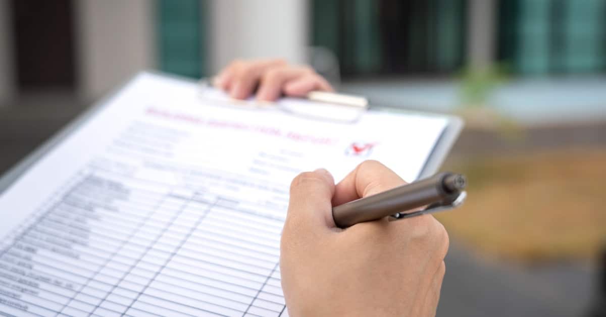 A close-up of a person's hand with a pen making marks on an inspection checklist attached to a clipboard.