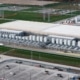 An aerial view of a large data center campus during the day with numerous cooling units, grass fields, and parking lots.