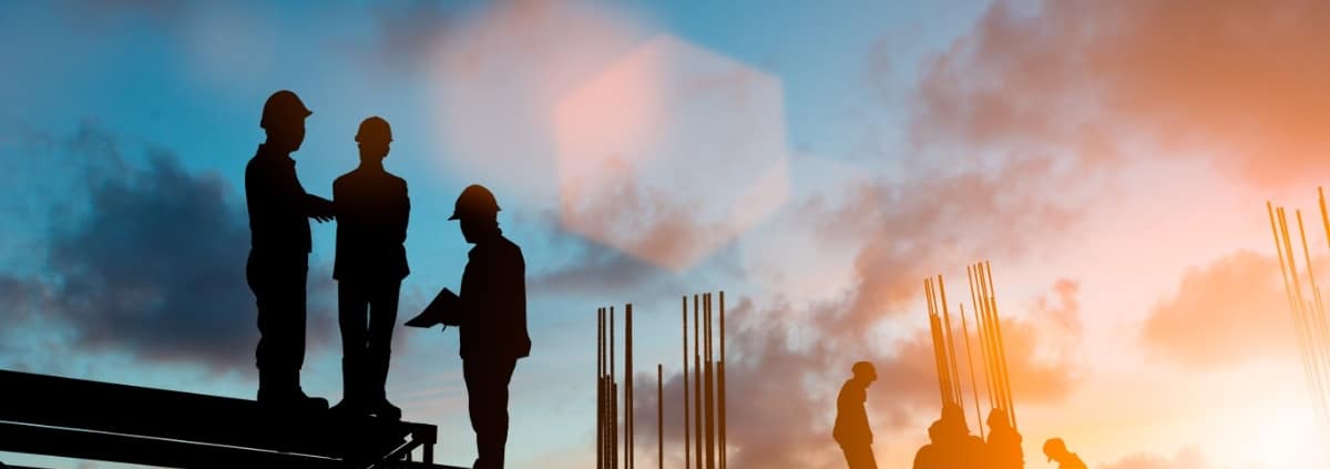 A silhouette of a construction site scaffolding with workers standing on platforms as the sun sets behind them.
