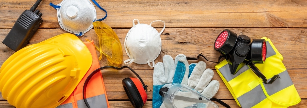 An overhead view of a wooden table with various construction safety equipment, including a hard hat, gloves, and goggles.