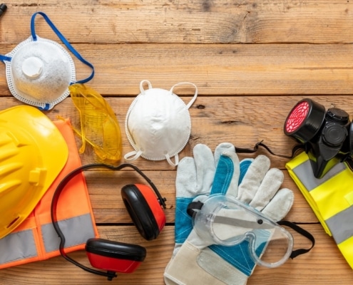 An overhead view of a wooden table with various construction safety equipment, including a hard hat, gloves, and goggles.