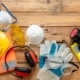 An overhead view of a wooden table with various construction safety equipment, including a hard hat, gloves, and goggles.