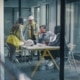 A group of men and women, some in business attire, others in construction attire, talk in a glass conference room.