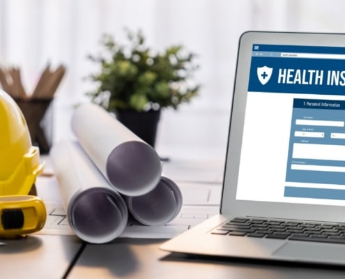 A laptop that displays an online health insurance form on its screen next to a hard hat and construction supplies.