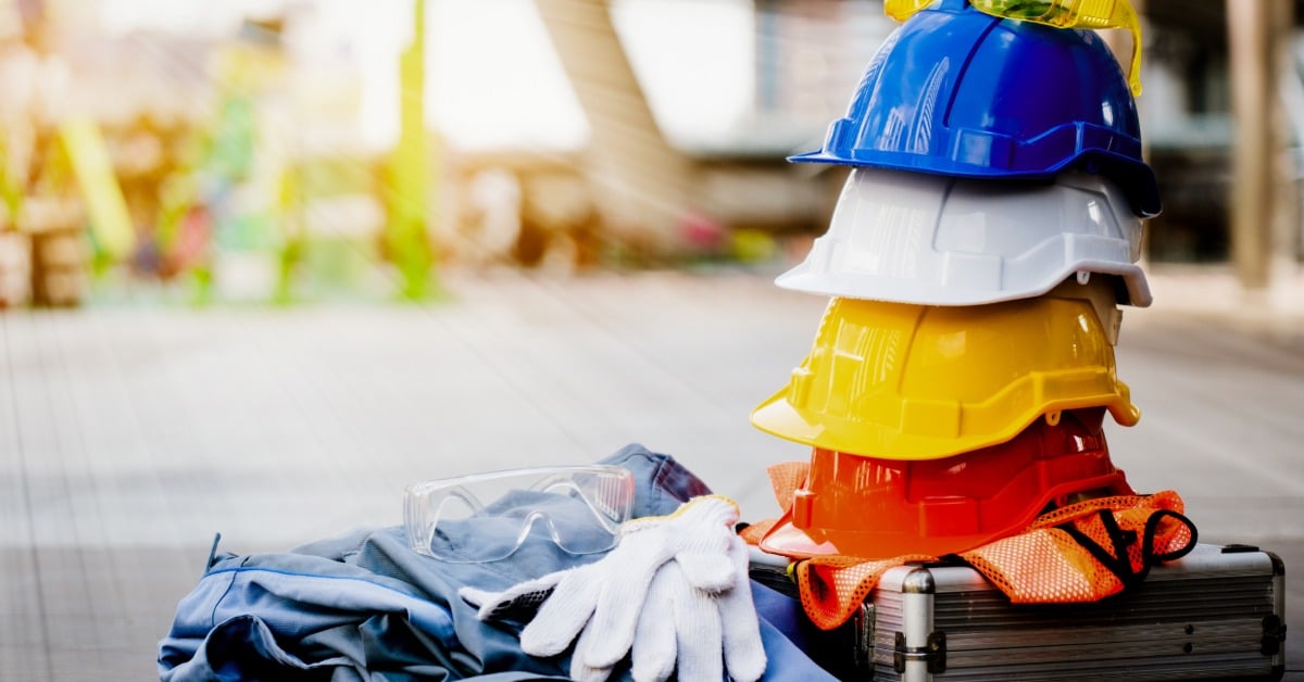 A pile of personal protective equipment for construction workers, including a stack of hard hats, safety goggles, and gloves.