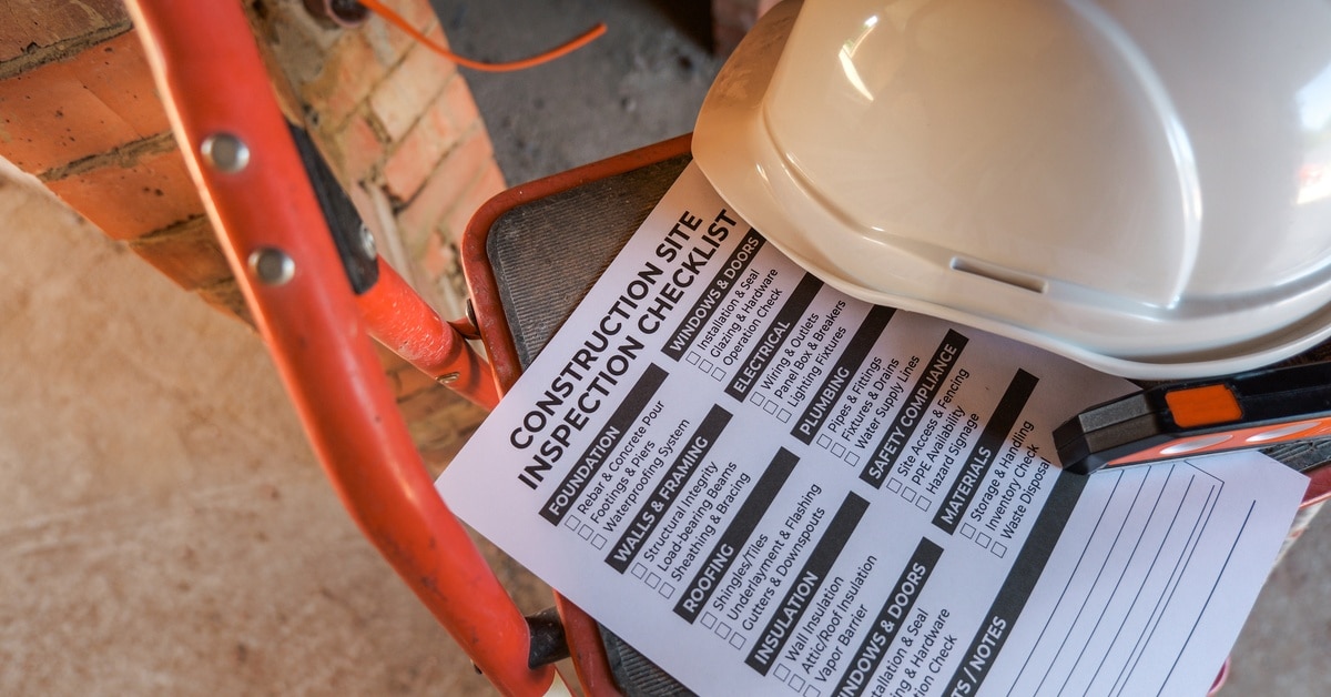 A close-up of a piece of paper on a stepladder next to a hard hat that reads "CONSTRUCTION SITE INSPECTION CHECKLIST."