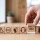 A close-up of a set of wooden blocks with various icons, with a hand pulling out one that reads "SAFETY FIRST."
