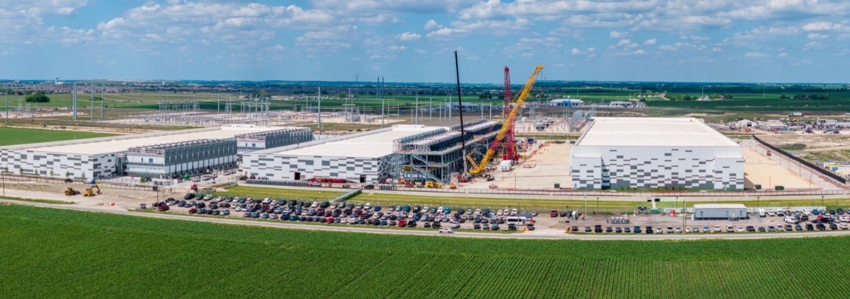 An aerial, landscape view of a large, multi-building data center under construction next to a green crop field.