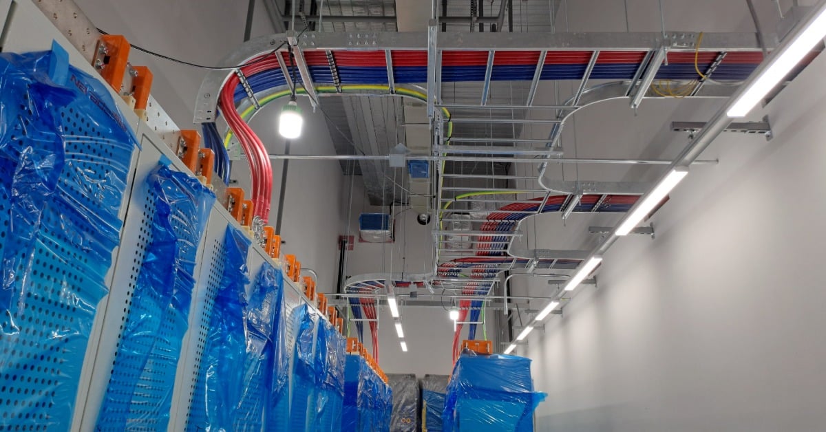 A view looking up at the electrical wiring and cable trays of a data center battery room under construction.