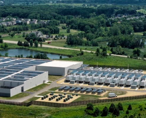 An aerial view of a large data center with solar panels on the roof, with residential houses in the background.