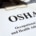 A close-up of a clipboard with a stack of papers attached to it, with the top one reading "OSHA" next to safety equipment.