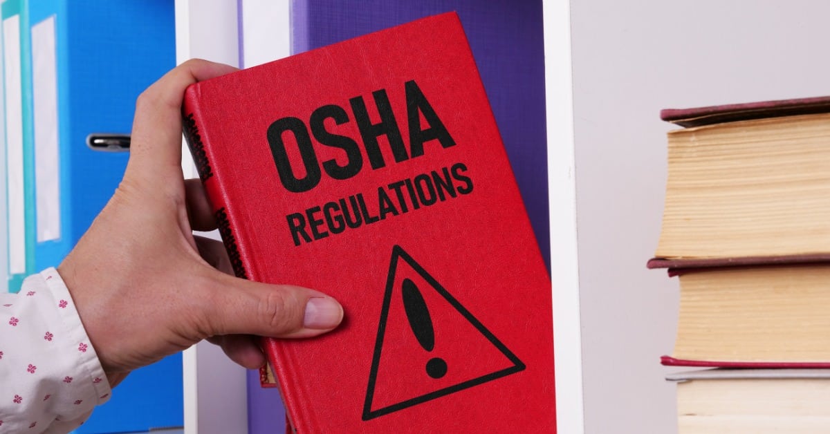 A close-up of a hand pulling a red hardcover book off a bookshelf with black font that reads "OSHA REGULATIONS."