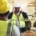 A group of men in high-visibility vests and hard hats is standing in a circle while a man touches his white helmet.
