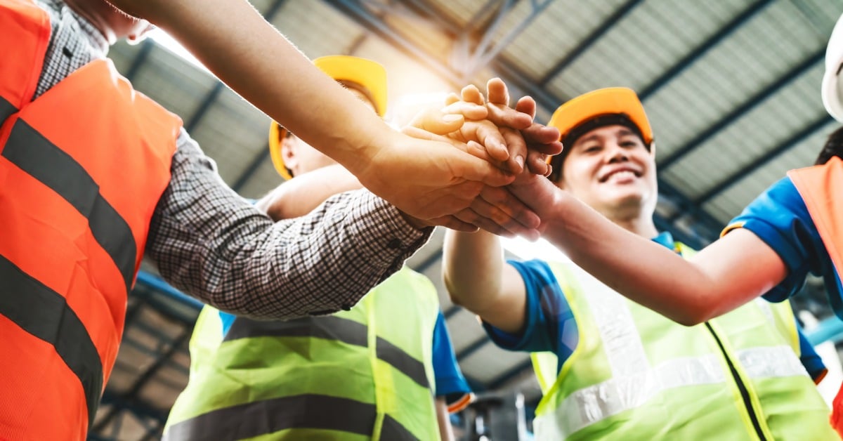 A view from below of a group of people in high-visibility vests standing in a circle and putting their hands in the middle.